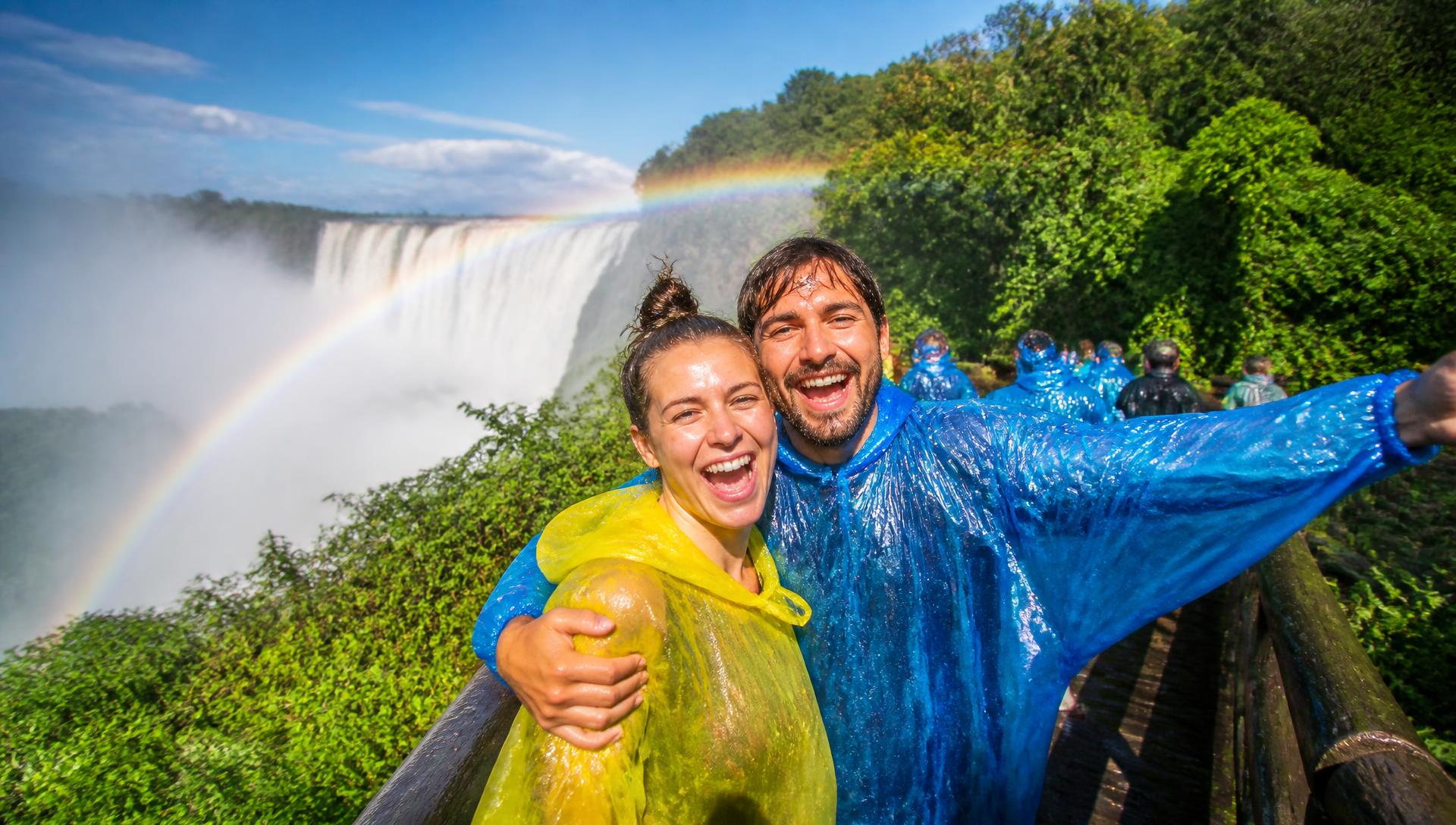 Delighted travellers in ponchos with a rainbow over Victoria Falls